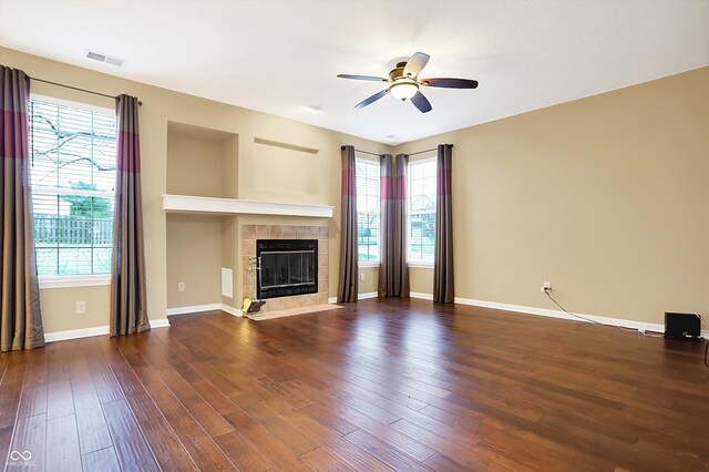 unfurnished living room featuring a tile fireplace, dark wood-type flooring, ceiling fan, and a healthy amount of sunlight