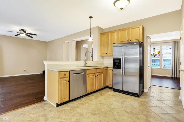 kitchen featuring appliances with stainless steel finishes, light wood-type flooring, ceiling fan with notable chandelier, sink, and hanging light fixtures