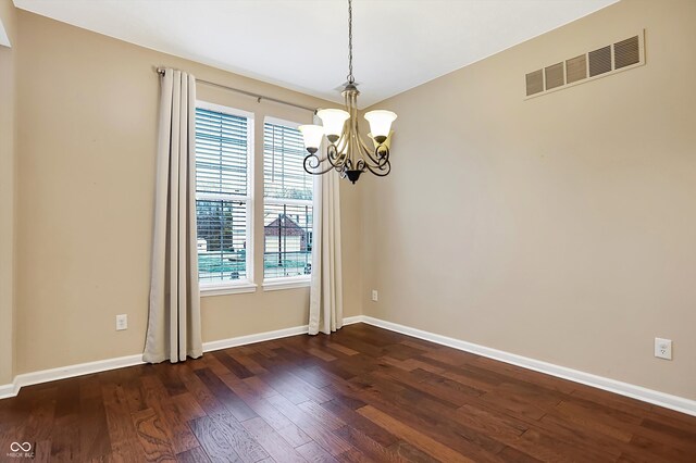 spare room featuring dark wood-type flooring and an inviting chandelier