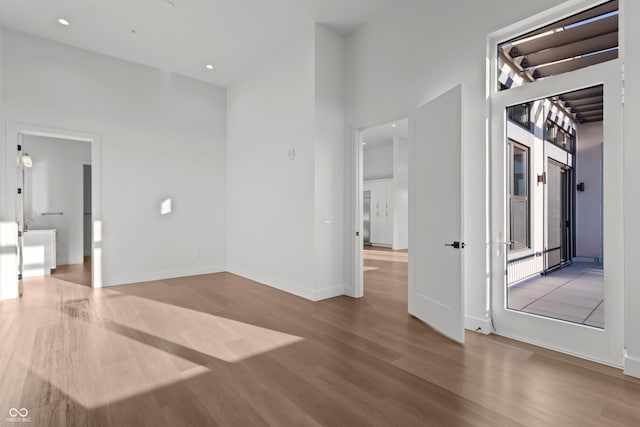 unfurnished room featuring a high ceiling, recessed lighting, wood finished floors, and baseboards