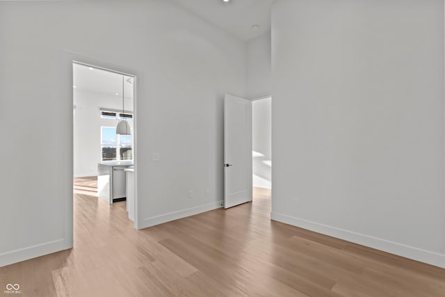 unfurnished room featuring light wood finished floors, a high ceiling, and baseboards