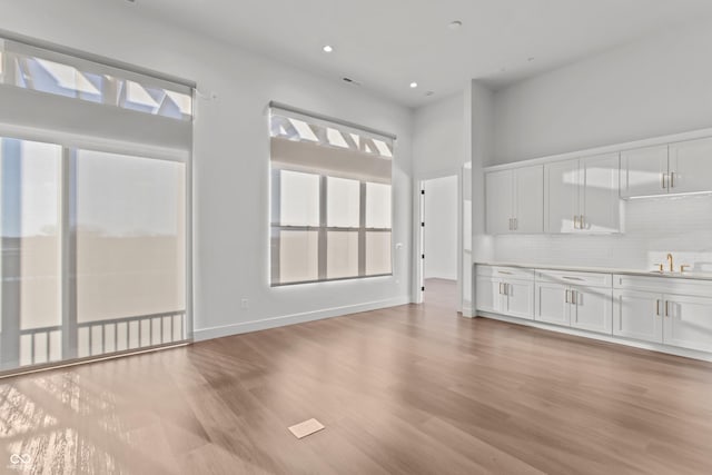 unfurnished living room featuring recessed lighting, baseboards, a sink, and light wood finished floors