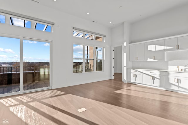 unfurnished living room with recessed lighting, baseboards, a towering ceiling, and light wood finished floors