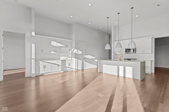 kitchen with a kitchen island with sink, stainless steel microwave, a towering ceiling, and decorative backsplash