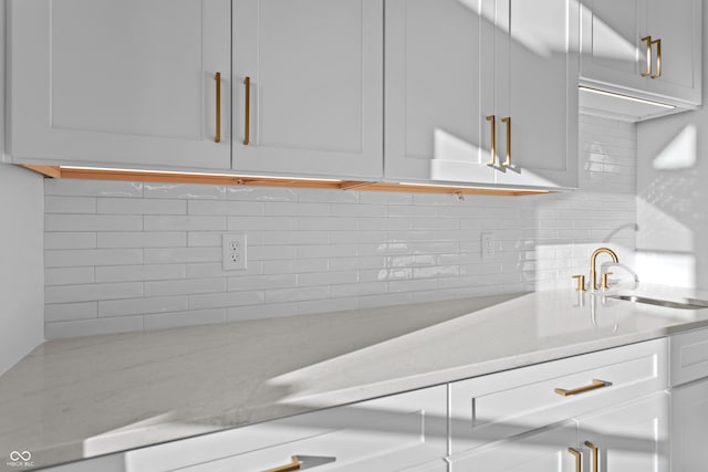 kitchen featuring tasteful backsplash, white cabinetry, light countertops, and a sink