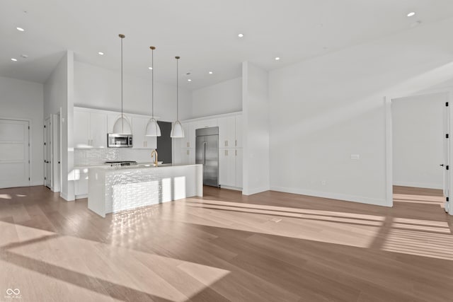 kitchen featuring a center island with sink, appliances with stainless steel finishes, a towering ceiling, and white cabinets