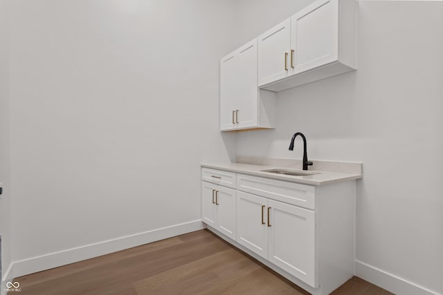 bar featuring light wood-style floors, baseboards, and a sink