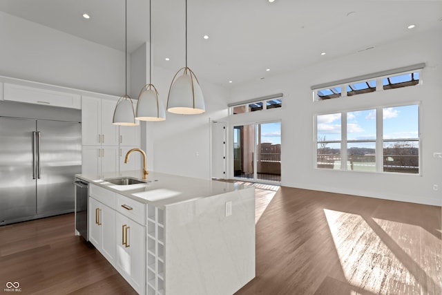 kitchen featuring a kitchen island with sink, a sink, dark wood finished floors, white cabinetry, and appliances with stainless steel finishes