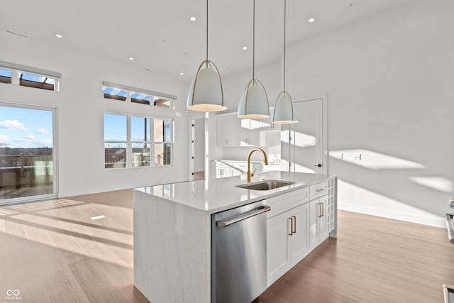 kitchen featuring an island with sink, a sink, stainless steel dishwasher, wood finished floors, and white cabinets