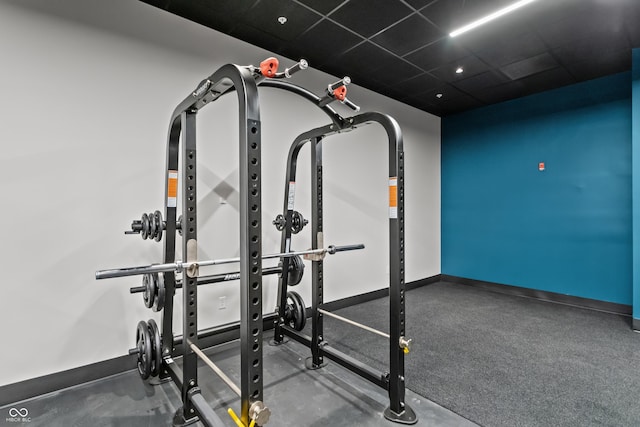 workout room featuring a paneled ceiling and baseboards