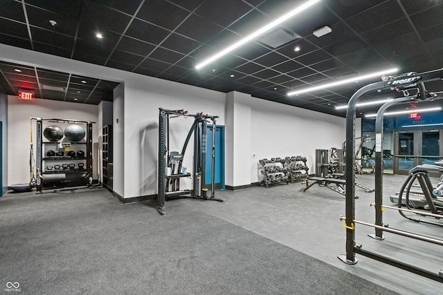 exercise room featuring a paneled ceiling and baseboards