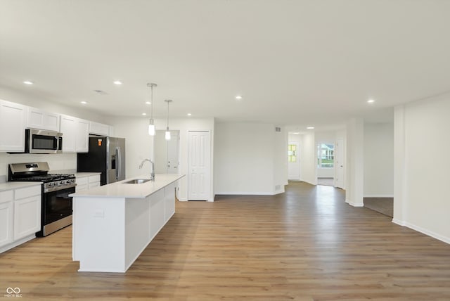 kitchen with a center island with sink, sink, pendant lighting, light wood-type flooring, and appliances with stainless steel finishes