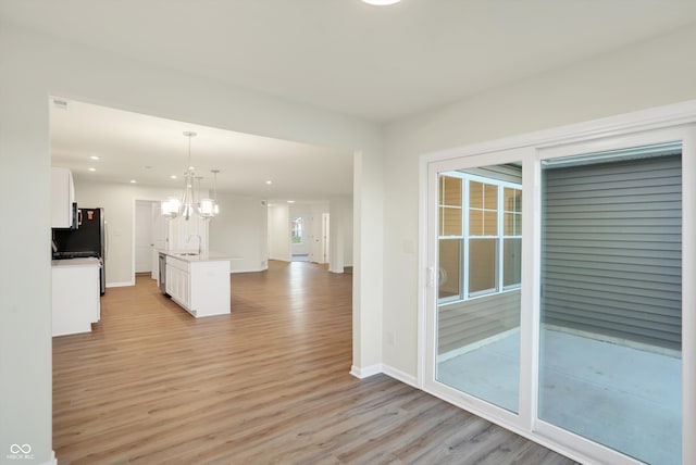 interior space featuring light hardwood / wood-style floors, white cabinetry, pendant lighting, and a kitchen island with sink