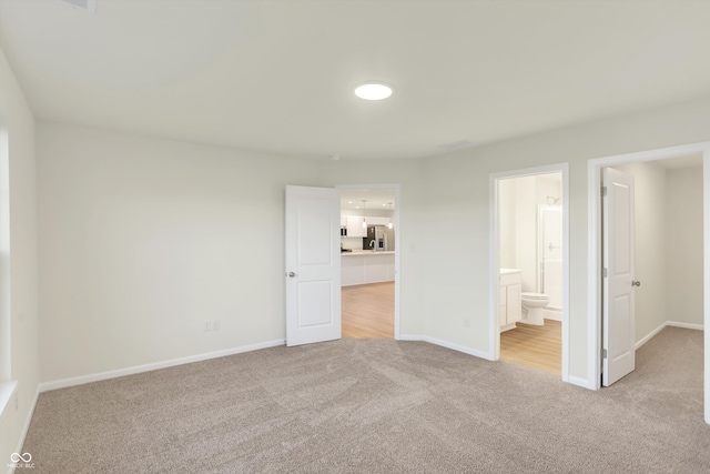 unfurnished bedroom with light colored carpet, stainless steel fridge, and ensuite bathroom