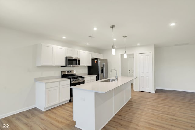 kitchen featuring stainless steel appliances, white cabinetry, pendant lighting, an island with sink, and light hardwood / wood-style floors