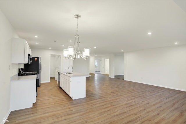 kitchen featuring white cabinetry, a center island with sink, sink, hanging light fixtures, and light wood-type flooring