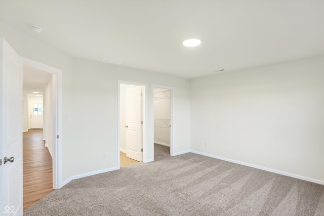 unfurnished bedroom featuring light colored carpet, a walk in closet, and a closet