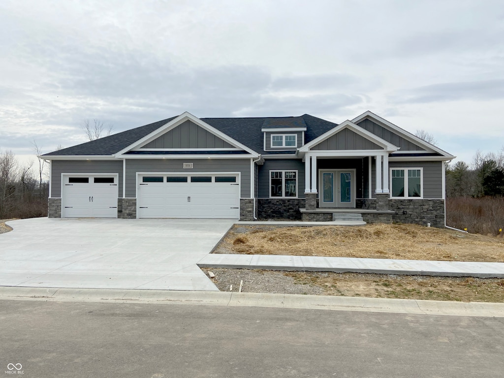 craftsman-style house featuring french doors, board and batten siding, a garage, stone siding, and driveway