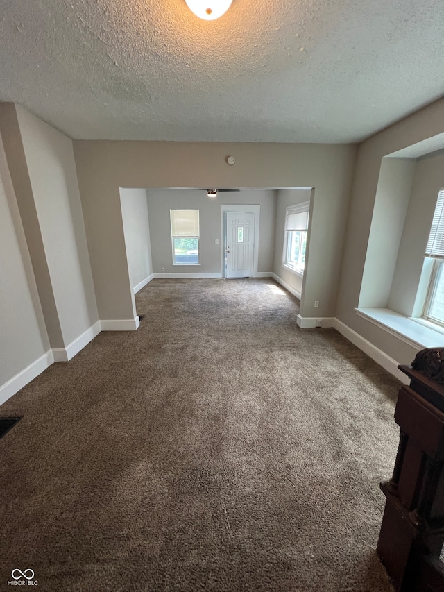 unfurnished living room featuring a textured ceiling, carpet floors, and a healthy amount of sunlight