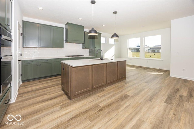 kitchen featuring custom exhaust hood, stainless steel appliances, a center island with sink, light hardwood / wood-style flooring, and hanging light fixtures