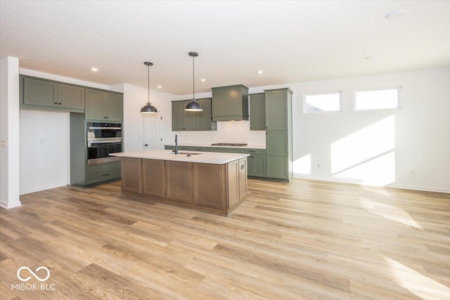 kitchen featuring sink, hanging light fixtures, a center island with sink, custom exhaust hood, and light wood-type flooring