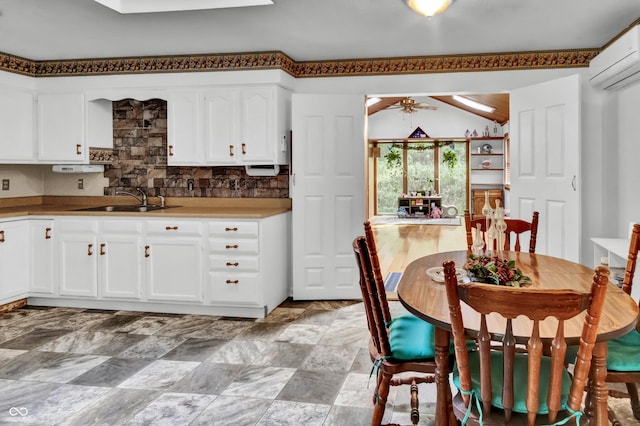 kitchen with an AC wall unit, a sink, backsplash, white cabinetry, and ceiling fan