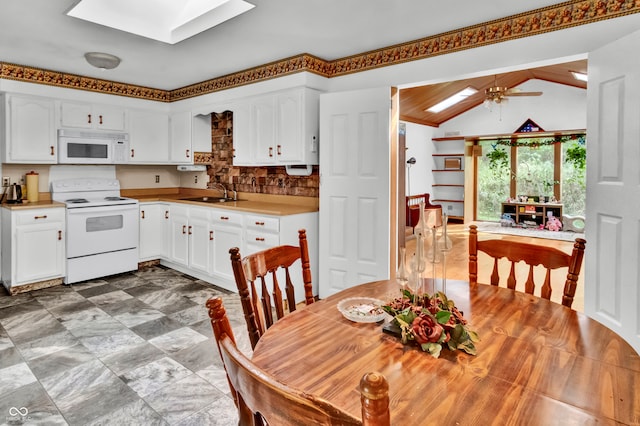 kitchen featuring white cabinets, ceiling fan, vaulted ceiling with skylight, and white appliances