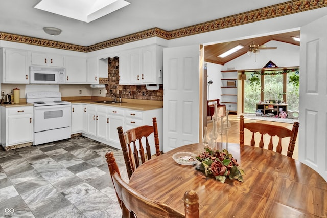 kitchen featuring lofted ceiling with skylight, a sink, decorative backsplash, white appliances, and white cabinetry