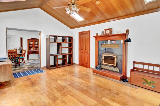 living room with a wood stove, ceiling fan, wooden ceiling, light hardwood / wood-style flooring, and vaulted ceiling with skylight