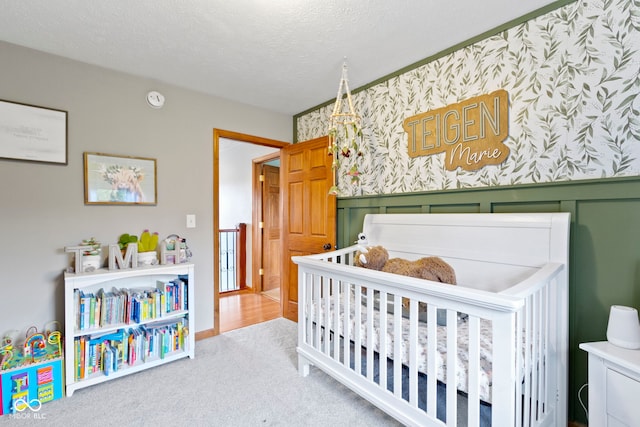 carpeted bedroom featuring a nursery area and a textured ceiling