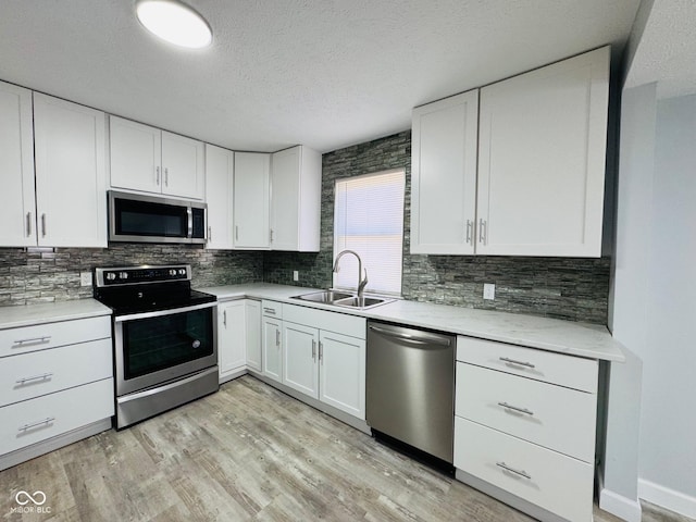 kitchen with stainless steel appliances, sink, white cabinets, and light hardwood / wood-style flooring