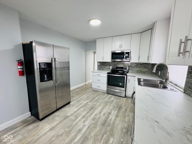 kitchen with sink, white cabinets, backsplash, stainless steel appliances, and light wood-type flooring