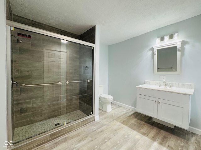 bathroom with a shower with door, hardwood / wood-style floors, vanity, a textured ceiling, and toilet