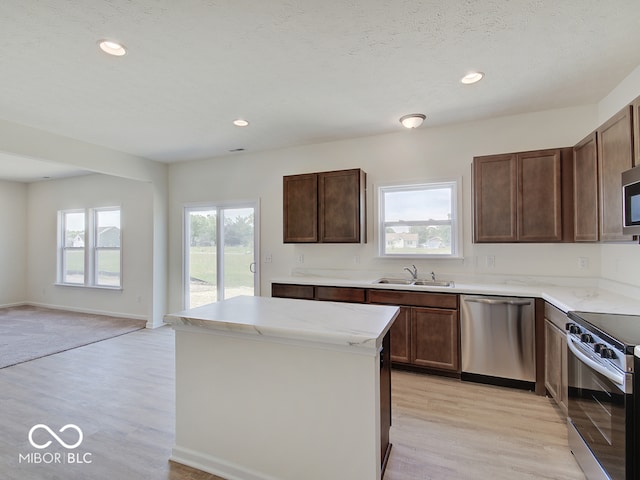 kitchen with sink, a center island, light hardwood / wood-style flooring, a textured ceiling, and appliances with stainless steel finishes