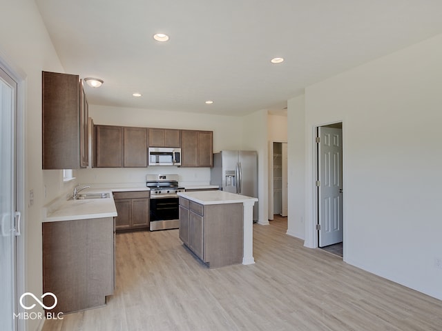 kitchen with sink, light hardwood / wood-style flooring, a kitchen island, and appliances with stainless steel finishes