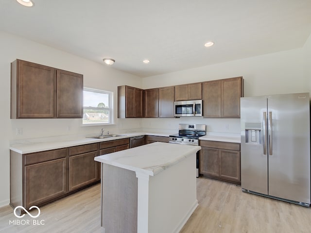 kitchen with dark brown cabinetry, stainless steel appliances, sink, a center island, and light hardwood / wood-style floors