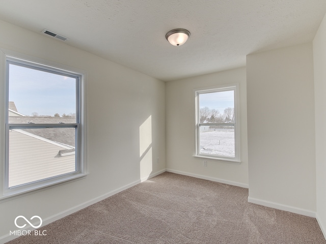 spare room featuring baseboards, visible vents, a textured ceiling, and light colored carpet