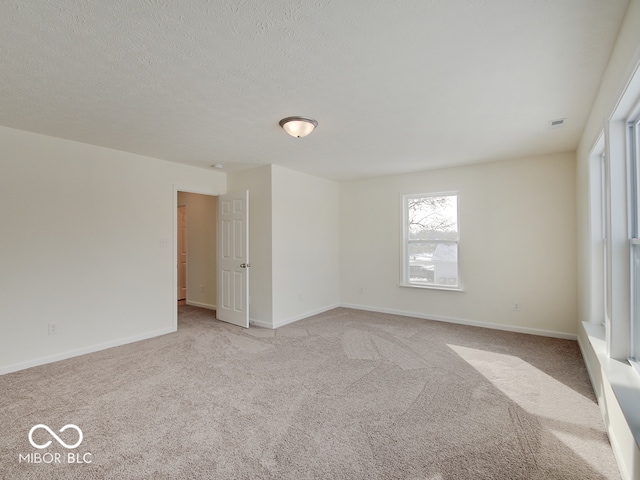 spare room with visible vents, baseboards, a textured ceiling, and light colored carpet