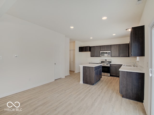 kitchen featuring stainless steel appliances, a sink, a kitchen island, light countertops, and light wood-type flooring