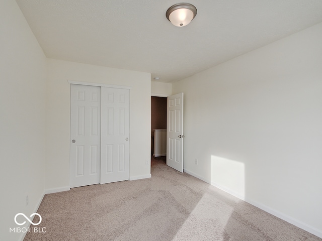 unfurnished bedroom featuring baseboards, a closet, and light colored carpet