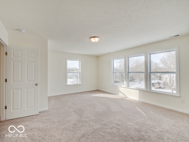 spare room featuring baseboards, visible vents, light carpet, and a textured ceiling