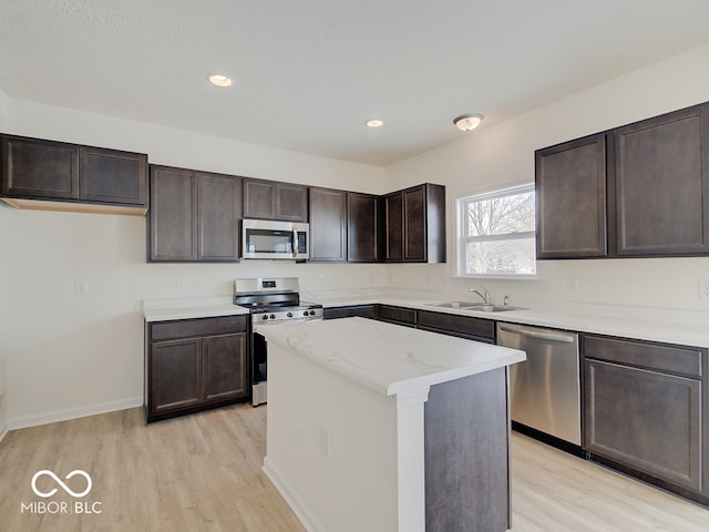 kitchen with a center island, light wood finished floors, stainless steel appliances, a sink, and dark brown cabinets