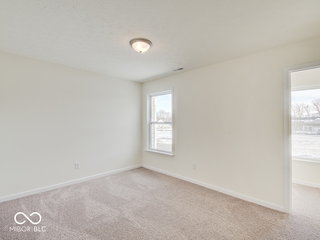 unfurnished room with light carpet, visible vents, baseboards, and a textured ceiling