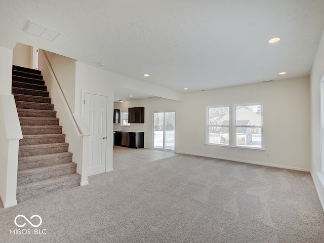 unfurnished living room featuring light carpet, stairway, a textured ceiling, and recessed lighting