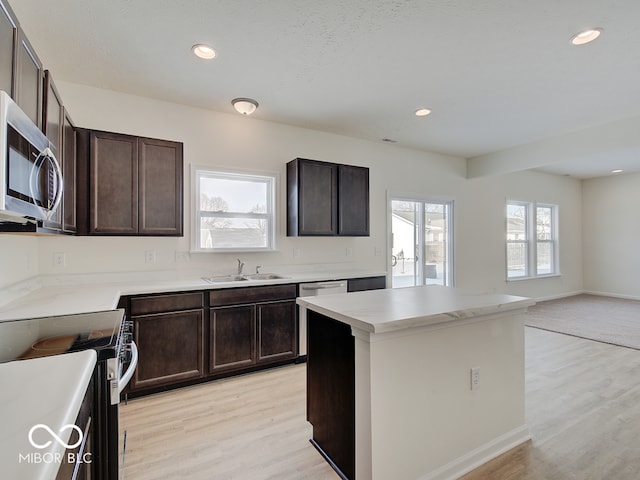 kitchen with light wood finished floors, stainless steel appliances, light countertops, a healthy amount of sunlight, and a sink