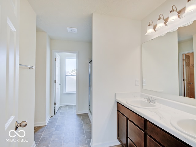 bathroom featuring double vanity, a stall shower, a sink, and baseboards