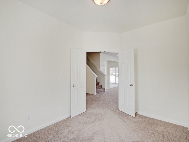 empty room with light carpet, stairs, and baseboards