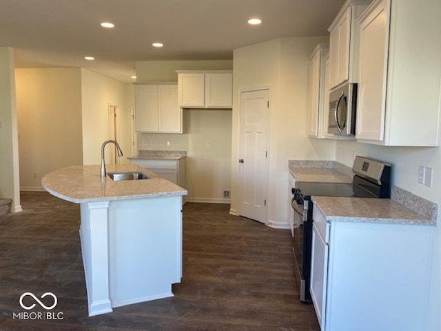 kitchen with appliances with stainless steel finishes, a kitchen island with sink, light stone countertops, white cabinets, and sink