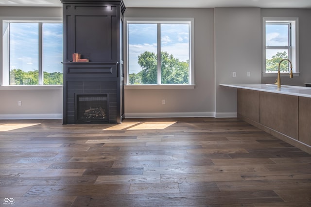 unfurnished living room featuring a large fireplace, dark wood-style flooring, a sink, and baseboards