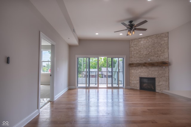 unfurnished living room featuring ceiling fan, a stone fireplace, baseboards, and wood finished floors